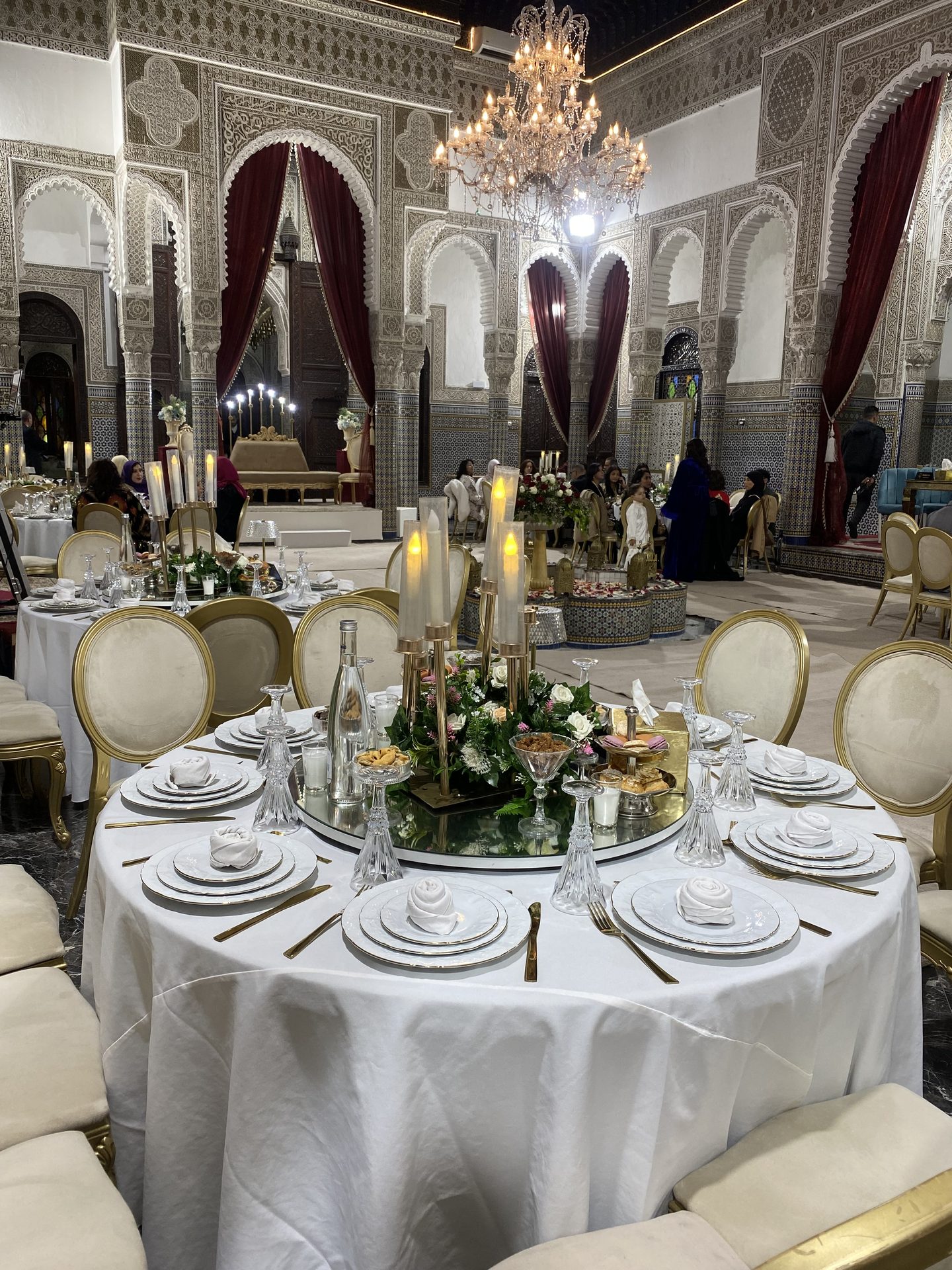 Table blanche dressée dans un riad sous un lustre, arcades en zellige