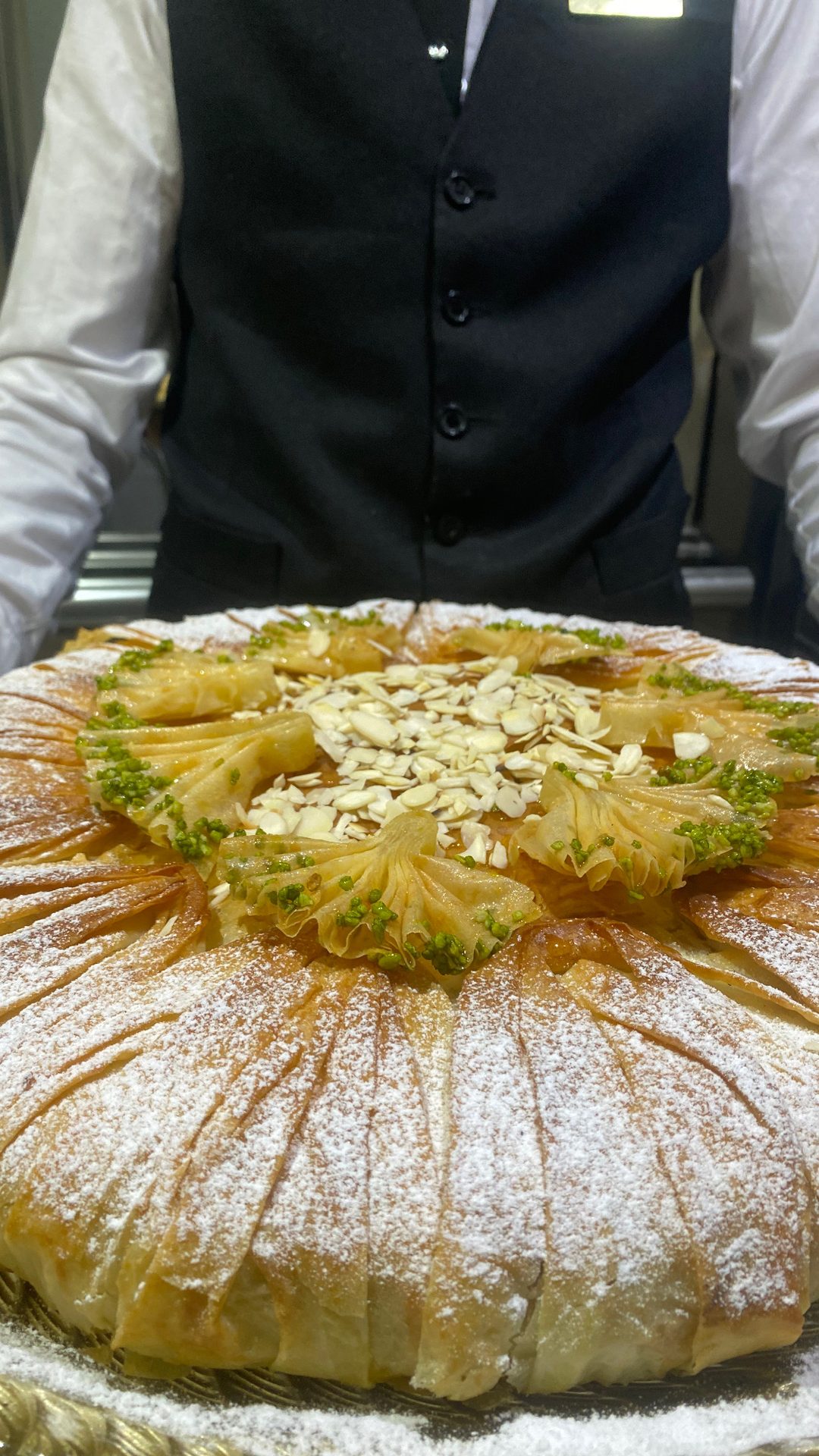 Serveur présentant une grande m'hencha aux amandes et pistaches