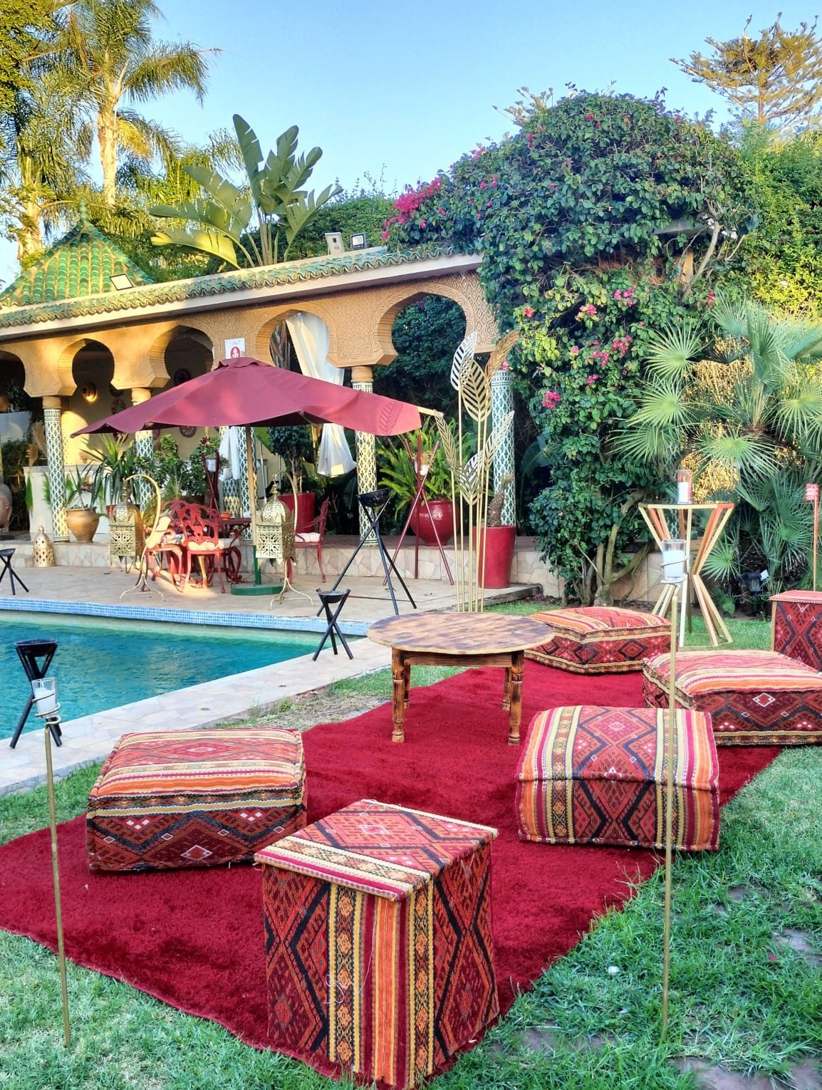 Salon marocain extérieur : poufs berbères et tapis au bord de la piscine